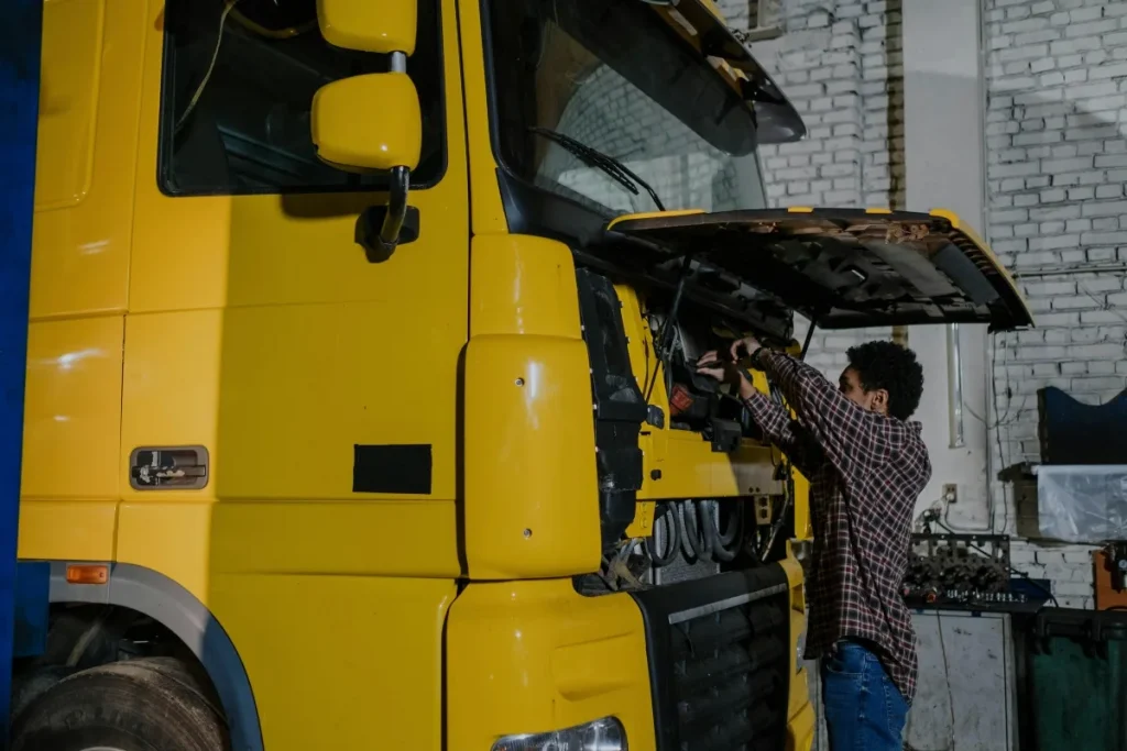 Mechanic repairing a yellow transport truck.