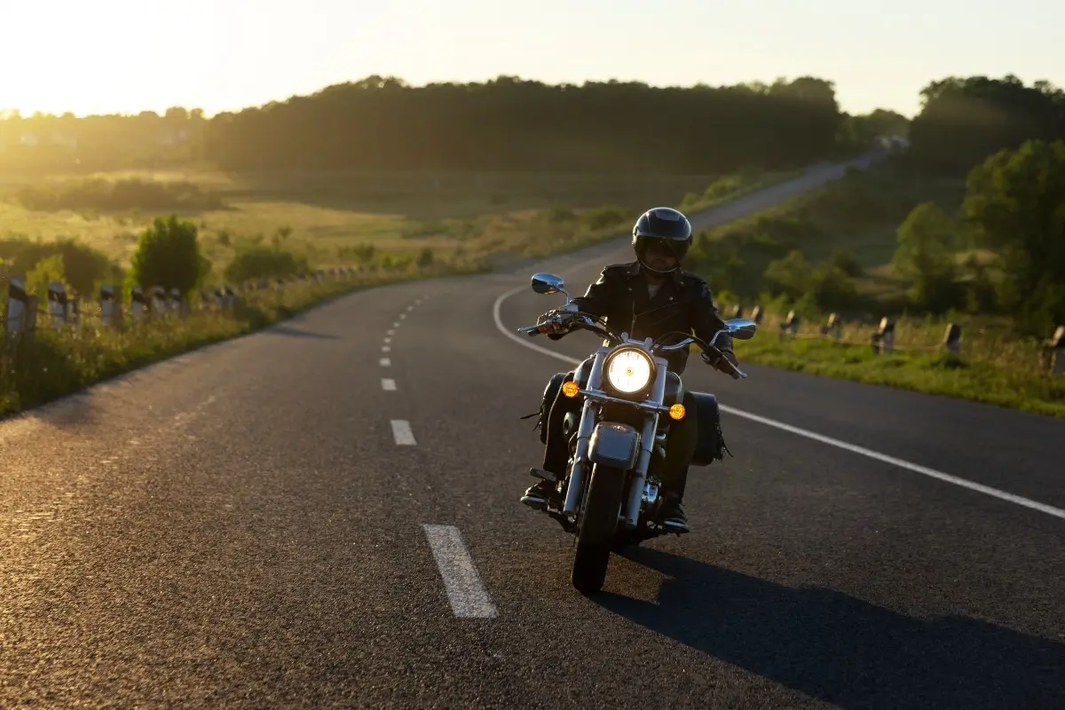 Motorcyclist riding along a winding country road at sunset.