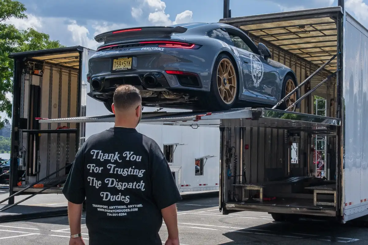 Gray Porsche being loaded into an enclosed transport trailer.
