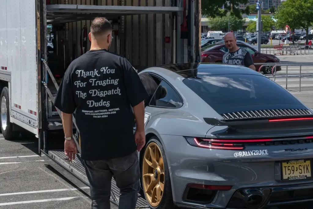 Person supervising a gray Porsche being loaded into an enclosed transport trailer.