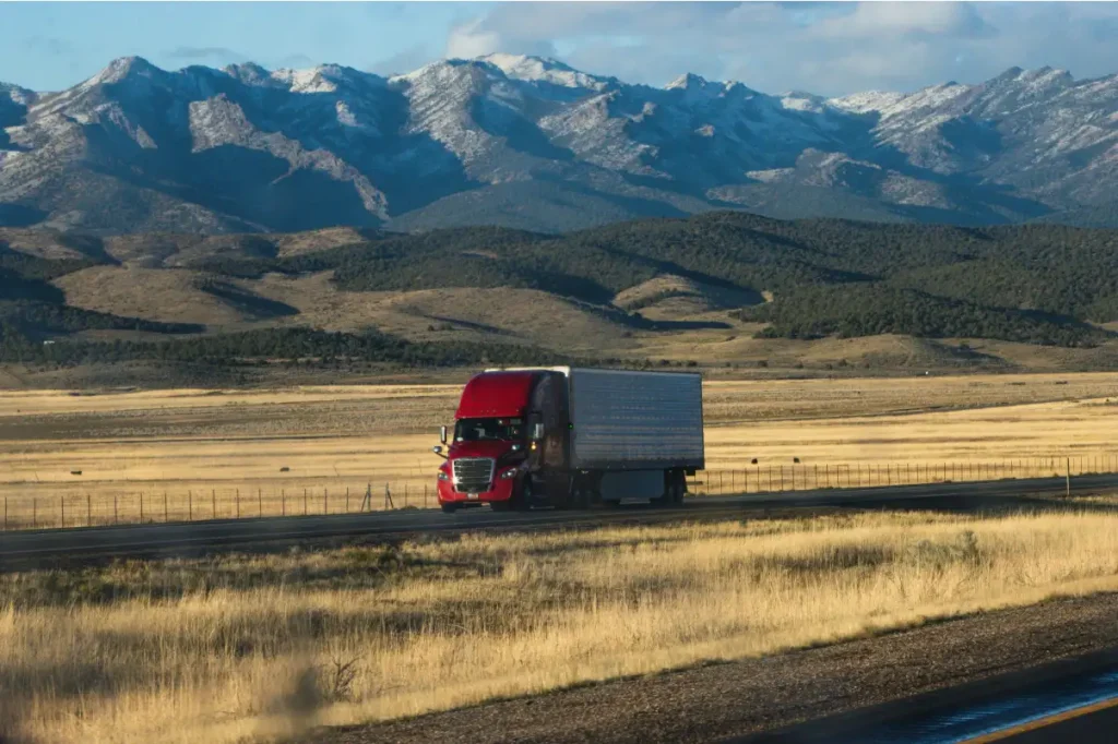 Red truck driving along a highway through a mountain landscape.