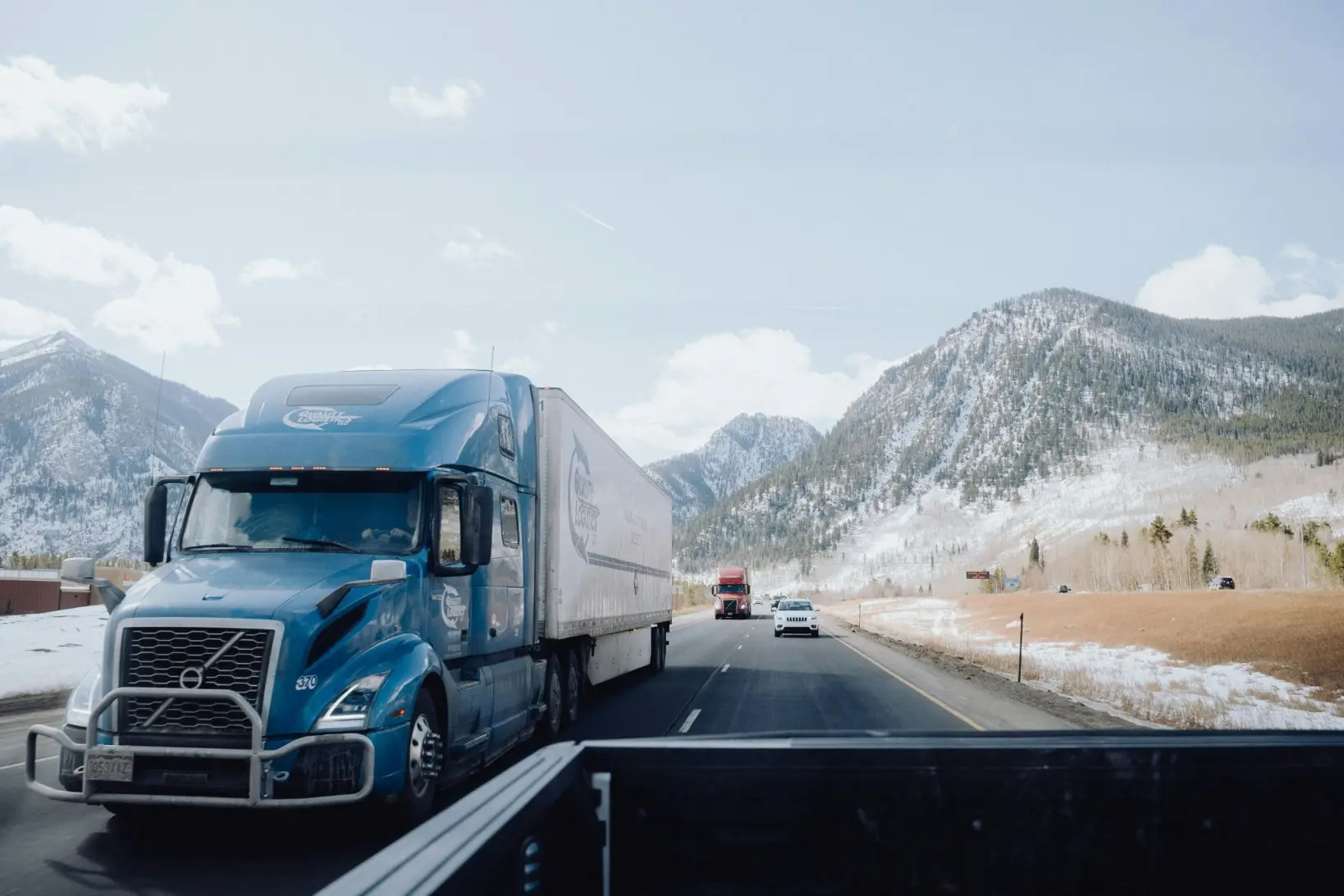 A truck transporting cars over mountains in the winter.