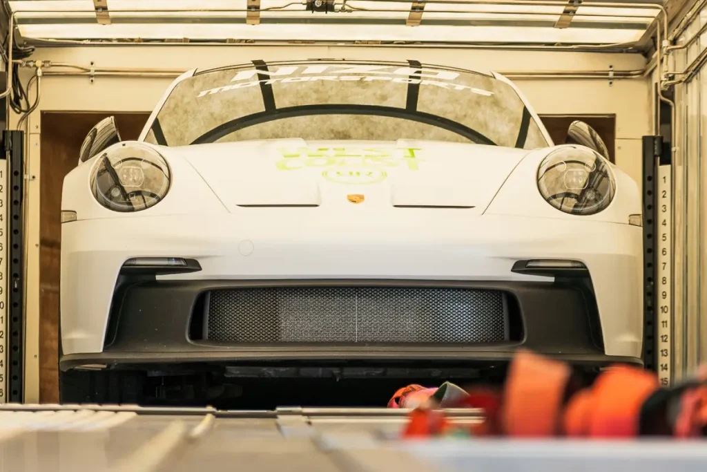 White Porsche positioned inside an enclosed transport trailer.