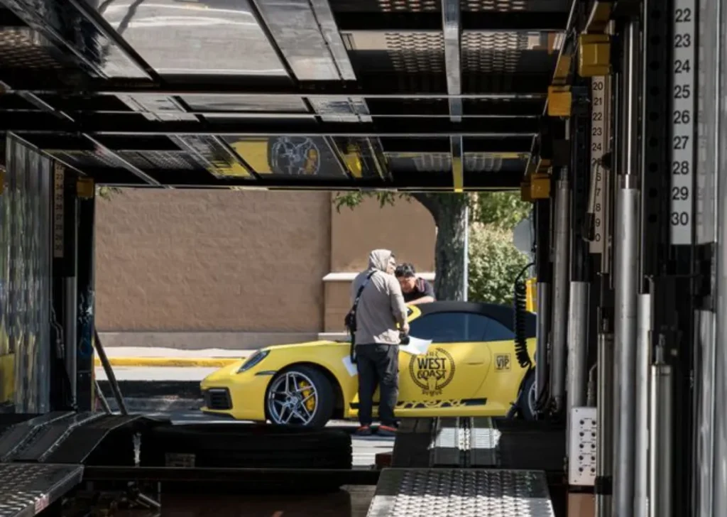 A person beside a yellow car inside an enclosed trailer.