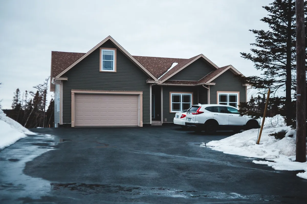 A small residential house with cars parked on snowy ground in a misty neighborhood, illustrating transport challenges.